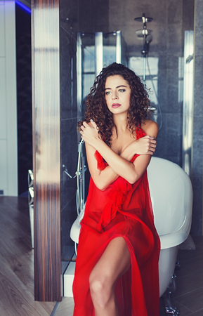 Beautiful curly model in red dress posing indoorの写真素材