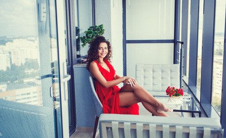 beautiful elegant woman in red dress sitting on balconyの写真素材