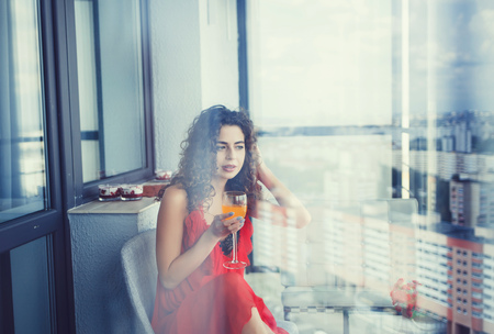 curly woman in red dress with a glass of juiceの写真素材