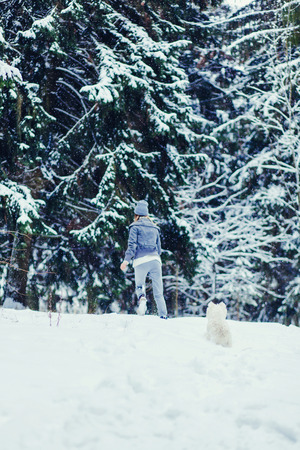young woman in a coat running around in the snow with her dogの写真素材