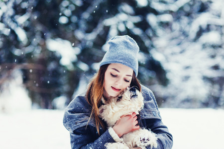 Portrait of beautiful young woman playing with dog in winter parkの写真素材
