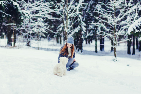smiling woman playing with dog in snowy weatherの写真素材
