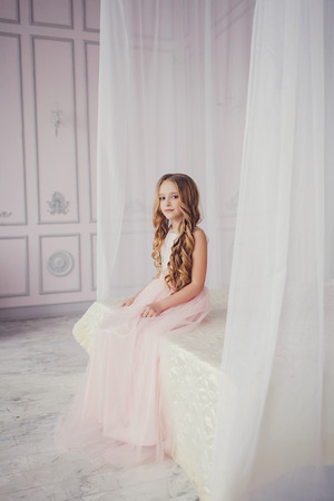 Full-length of little girl in dress sitting on bedの写真素材