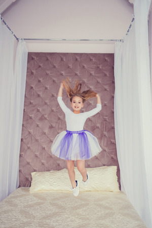 funny little cheerleader girl jumping on the bed in the studioの写真素材
