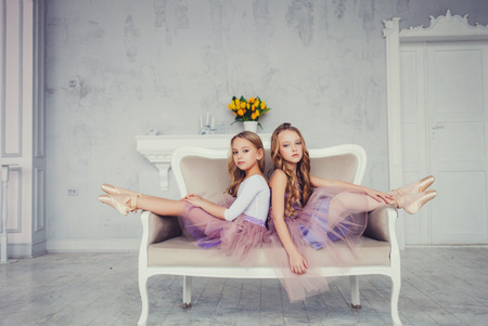 Two cute little girls ballerinas sitting on background in the studio. Two fashion sisters posing indoorsの写真素材