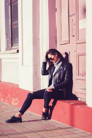 Stylish hipster girl in leather jacket sitting in urban space.Street fashion conceptの写真素材