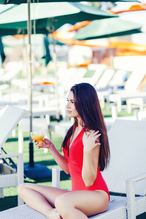 brunette woman with a glass of juice sitting under a chaise longue and restingの写真素材