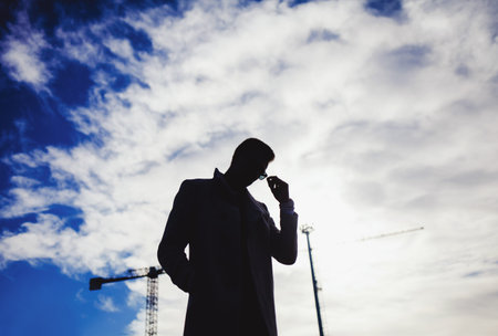 silhouetted man in sunglasses standing on blue sky background
