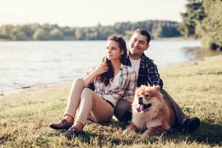 Young happy couple of man and woman with chow chow dog sit at grass on sunny dayの写真素材