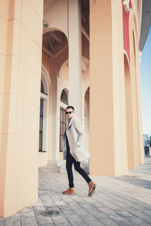 Fashionable handsome hipster man model with stylish sunglasses and coat in the cityの写真素材