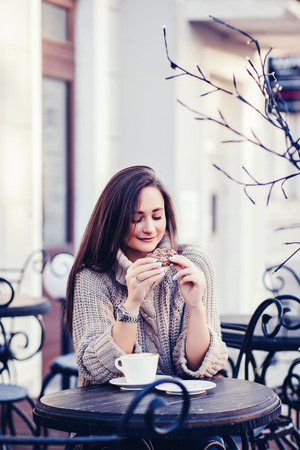 woman in sweater sitting in a cafe and holding coffee with biscuitsの写真素材