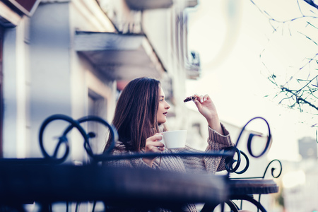 a young girl sits on the terrace of a cafe, drinking coffee with cookiesの写真素材