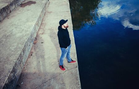 Hipster handsome male model with beard wearing black hoodie and cap in casual urban style の写真素材