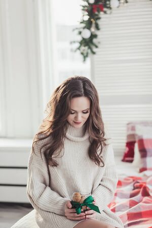 a beautiful woman in a warm sweater holds a jar of decorated cookiesの写真素材