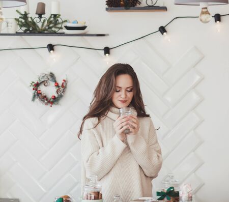 a beautiful woman in a warm wool sweater stands in the kitchen with a mugの写真素材