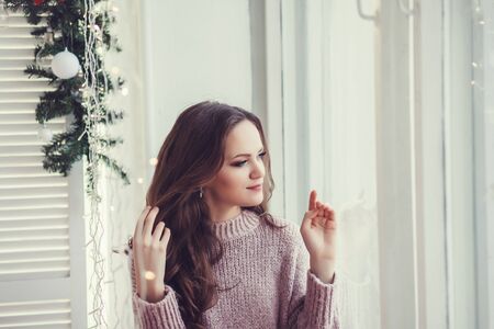 charming gorgeous girl in sweater sitting at Christmas windowの写真素材