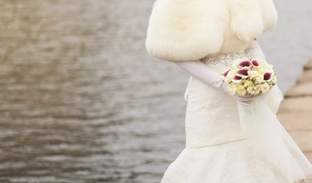 bride in a fur coat with a wedding bouquet on the background of the river. copy space