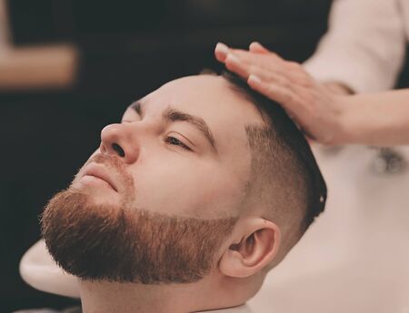 Barber washing bearded client's hair in barber shopの写真素材