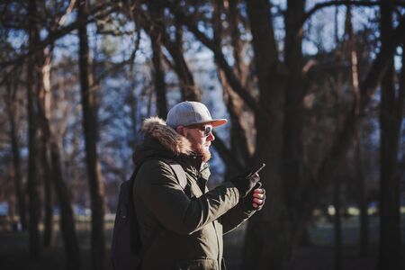 bearded man in a cap is holding a smartphone outdoorsの写真素材