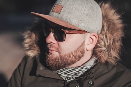 cool bearded man in cap and winter jacket outdoorsの写真素材