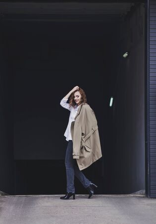 Young stylish girl wearing modern trench coat walking in urban city smiling happy.の写真素材