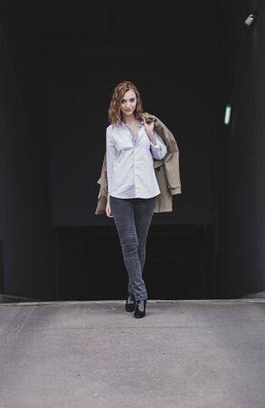 fashionable woman in a shirt and coat walks down the street and smilesの写真素材