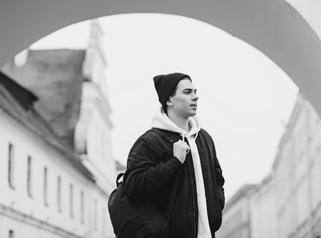 Stylish young man in black clothes and a white hoodie with a backpack in the cityの写真素材