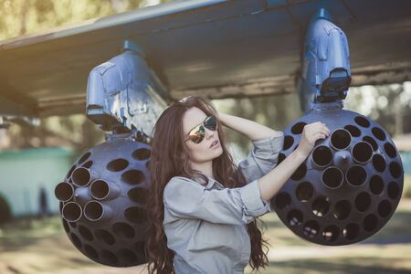 young woman poses near a military plane wearing Aviator glassesの写真素材