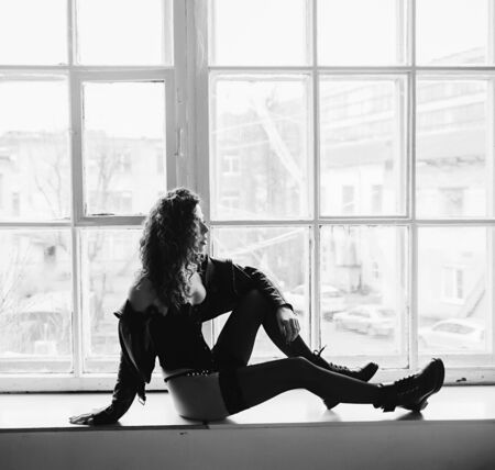 silhouette trendy woman in leather jacket and shoes in windowの写真素材