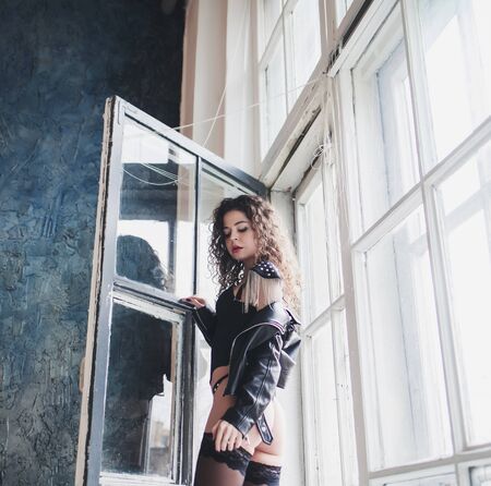 attractive long hair young woman in black leather jacket and stockings posing indoorsの写真素材