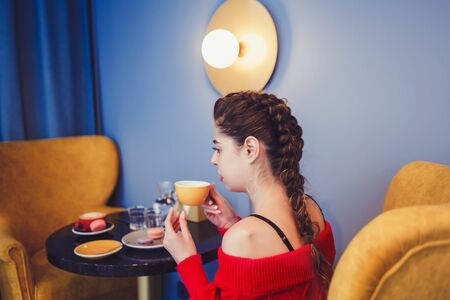 Young pretty cheerful woman sitting and drinking coffee in cafeの写真素材