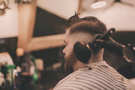 Hipster man getting haircut by hairdresser at the barbershopの写真素材