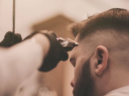 Close up of a hairdresser`s work for a handsome man at the barber shop. He is doing styling with the electric shaverの写真素材