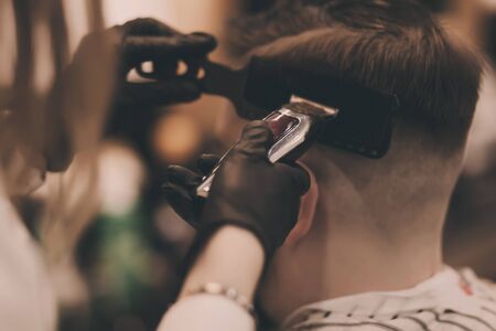 Young bearded guy at the barber shop. He is doing styling with the electric shaverの写真素材