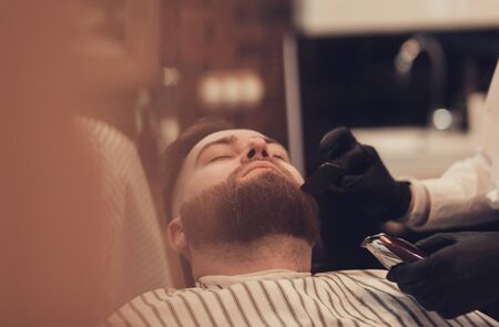 Barber cuts a man's beard with a comb and trimmerの写真素材
