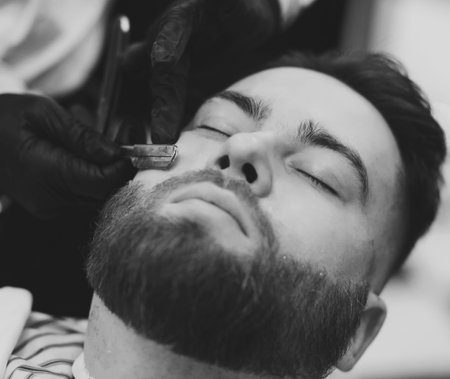 close-up of barber's hands with a dangerous razor shaves a man's beard in the salon