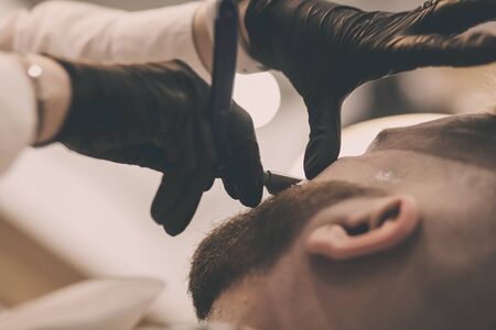 bearded man is getting shaved by hairdresser at the barbershopの写真素材