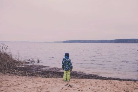  little boy stands on the shore of the lake and looks into the distance. rear viewの写真素材