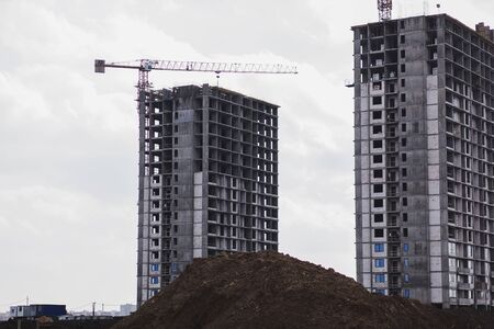building cranes at the background of a multi-storey building under construction. New houses for familiesの写真素材