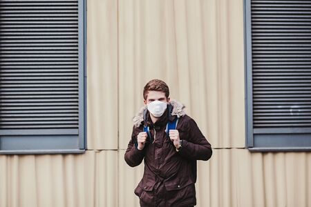 young man with a backpack in a protective mask from the flu. Concept of coronavirus quarantine.の写真素材