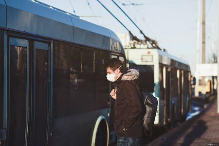 Young man wearing protective mask against transmissible infectious diseases and as protection against the flu near public transport. New coronavirus 2019-nCoVの写真素材