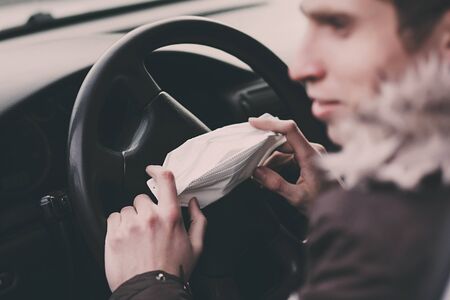 man holding protective mask in hand to avoid the infection of virus and polluted air spreading deseases inside of his car. Health care, coronavirus.の写真素材