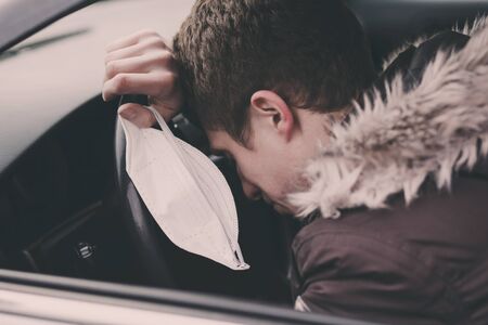 sick man rests behind the wheel in a car , holding a medical mask in his hand to protect against infection with coronavirus, a pandemicの写真素材