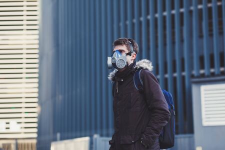 Young man with backpack wearing industrial mask in city. Coronavirus concept. Protect your health.の写真素材