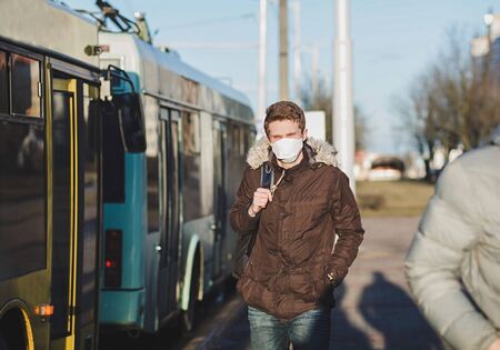 COVID-19 pandemic coronavirus a person near buses wearing a protective mask to spread the 2019 coronavirus disease. A man with a surgical mask on his face against SARS-cov-2.の写真素材