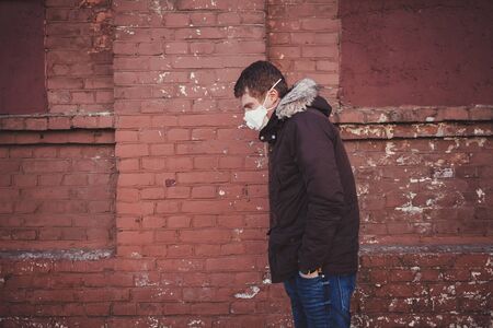 Ill sad man in protective mask near brick wall. air pollution and the epidemicの写真素材