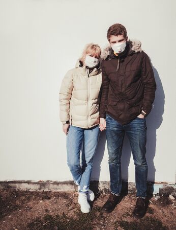 two people in protective masks hold hands against the wall. coronavirus pandemic and air pollutionの写真素材