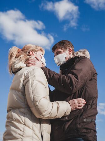 couple in love in jackets and medical masks hugs in sunny dayの写真素材