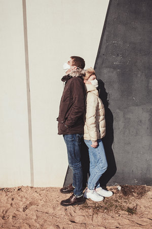 Couple in love, man and woman in protective medical mask standing together near wall.