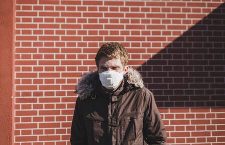 Caucasian man in medical mask standing near brick wall. Environmental pollution conceptの写真素材
